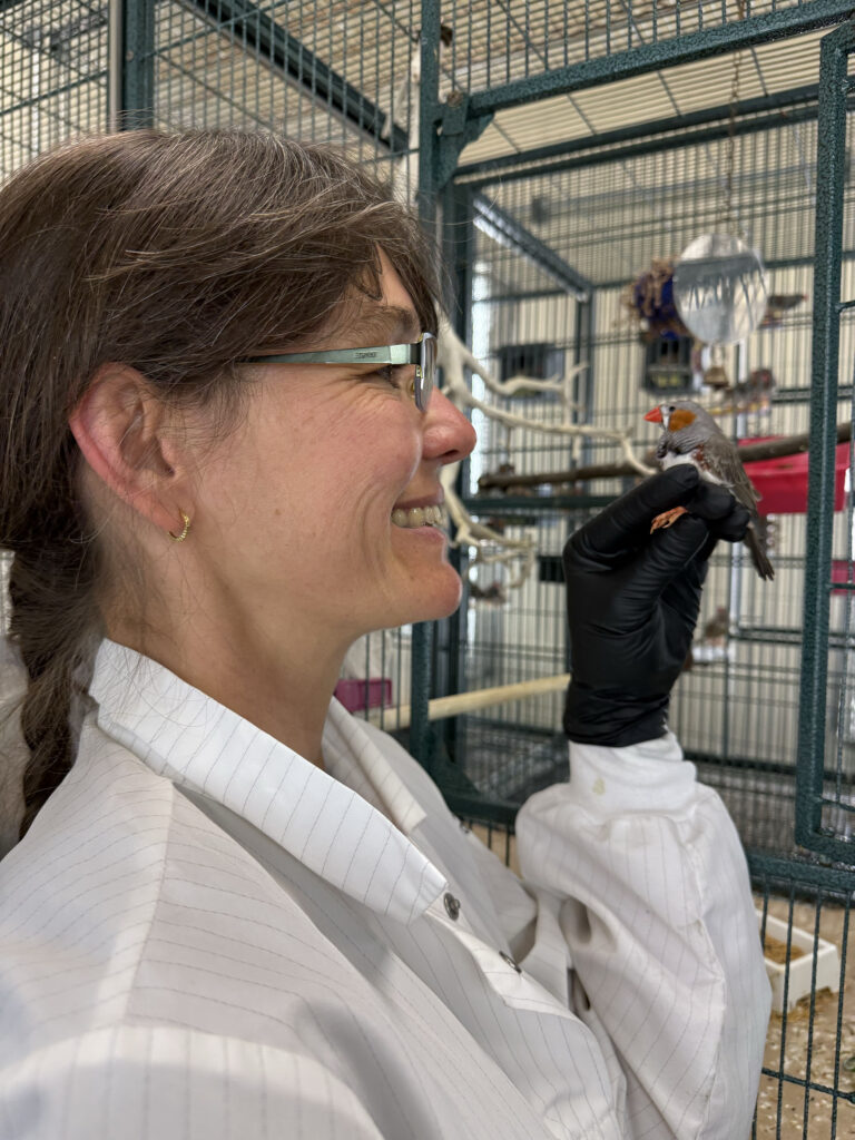 a smiling woman in white coat holding a small bird near its cage