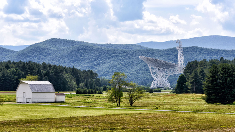 a radio telescope surrounded by grassy field and distant mountains