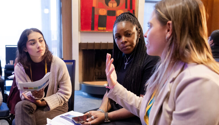 two women, left and center, listen to a third woman at right who is talking and gesturing