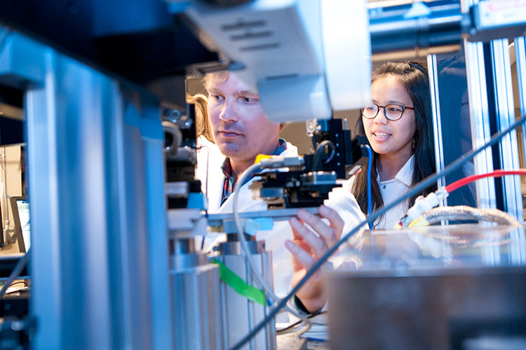 Two students stand behind some scientific equipment