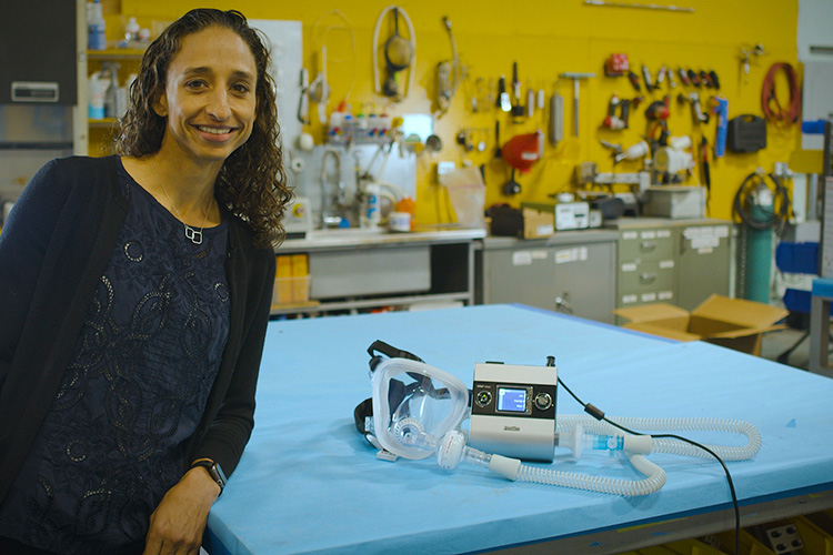 Associate professor Grace O'Connell stands next to a ventilator, which is lying on a table in her lab, that she created from a used sleep apnea machine