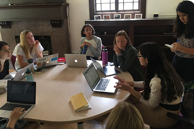 Students at UC Berkeley's Human Rights Center Investigations Lab sit at a round table, their laptops open, discussing their work.