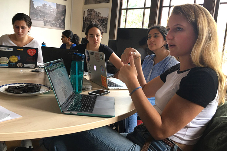 Students in the Human Rights Center Investigations Lab sit at a round table with their laptops and discuss their work.