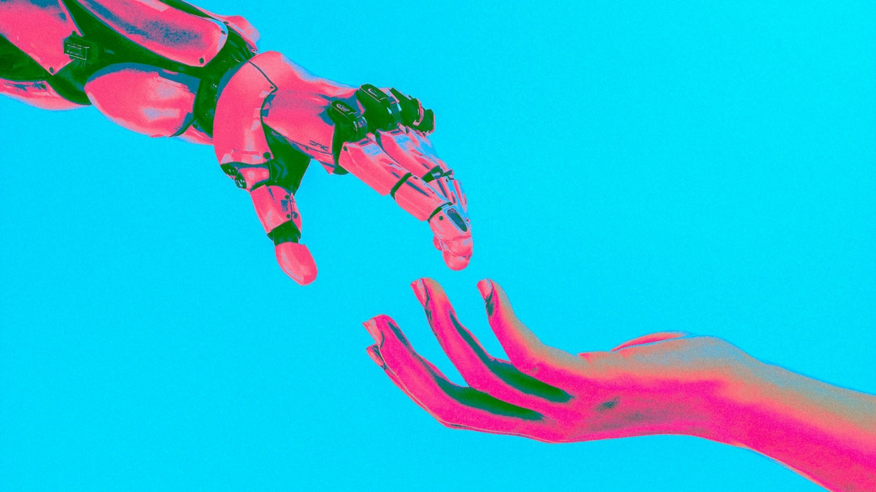 A pink robot hand and a pink human hand reach for each other against a blue background