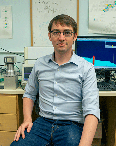 A photo of Jake Hecla sitting at a desk in front of a computer.