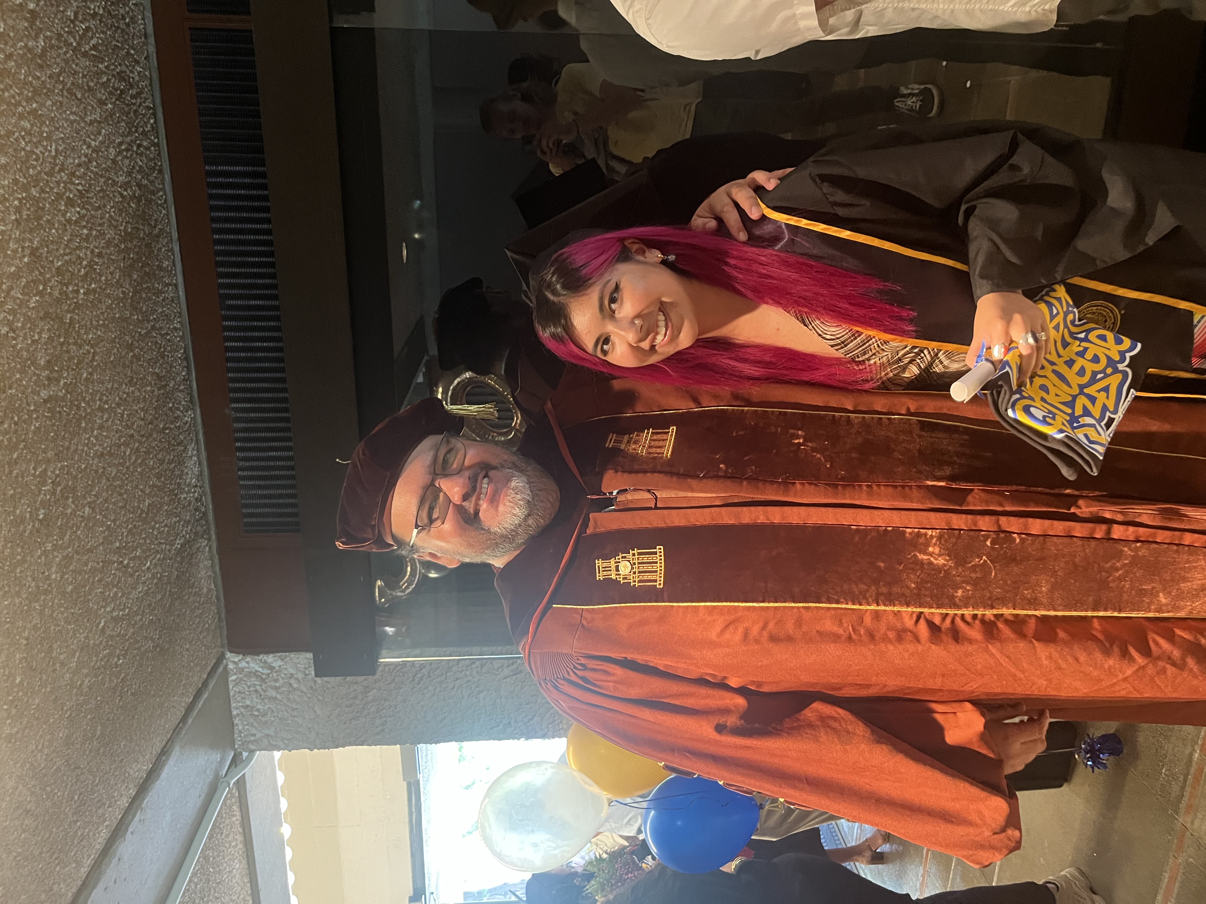 Pablo Gonzalez wearing a faculty graduation robe standing next to Ceclie Lopez during her graduation.