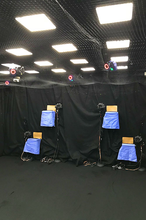 A photo of a room with black curtains on the walls, netting hanging from the walls and the ceiling, and a series of cameras on the walls and ceiling.
