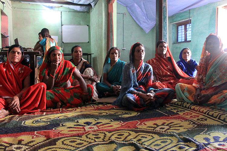 Indian woman at an educational meeting, sitting on the floor around a colorful patterned rug