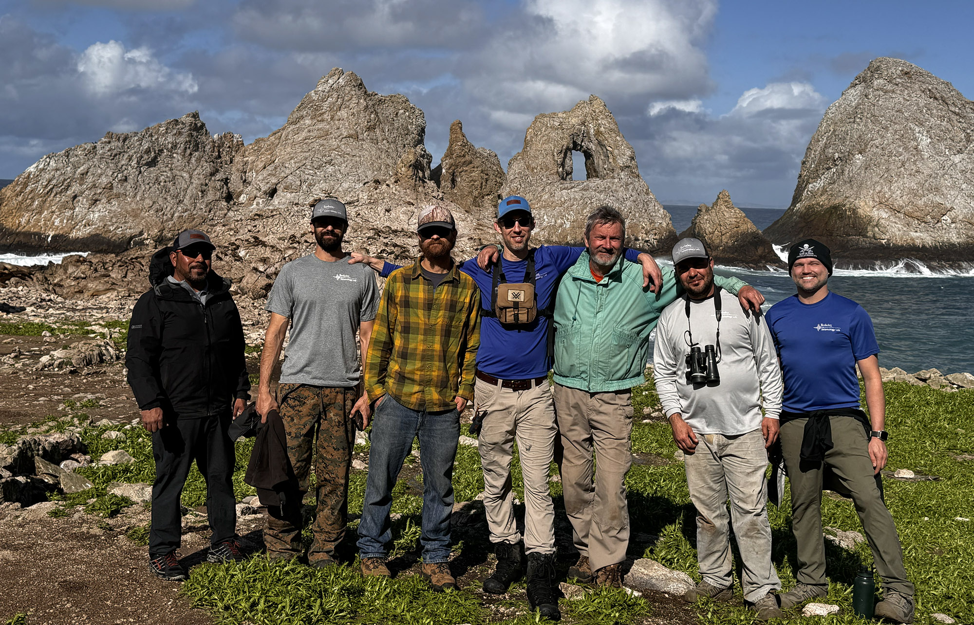 7 men smiling into the camera with rugged rocks in the background