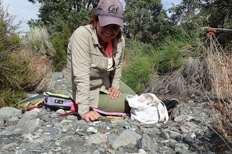 Jenna Ekwealor sitting on the ground among rocks, deploying equipment to measure conditions under rocks