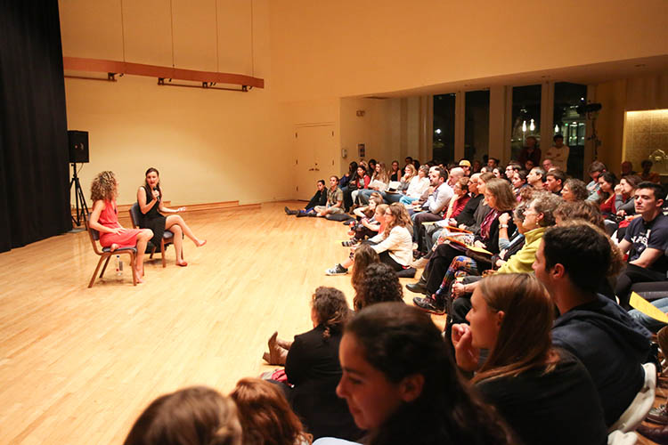 two women speak on stage in front of a group of people