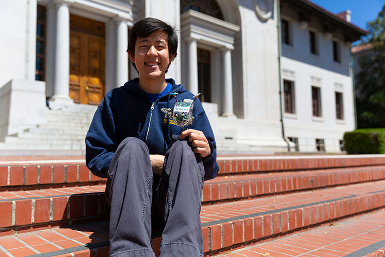 Justin Yim sits on steps holding a small robot