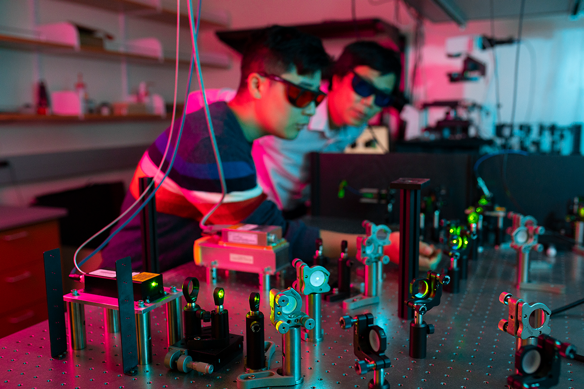 Ke Yu with Alex Choi in lab, red light surrounds them as they sit at a table of instruments.