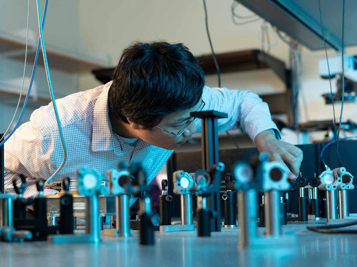 Ke Yu in lab with instrumentation in the foreground.