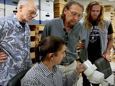 a group of four men (identified in the caption) stand around a microscope in a lab