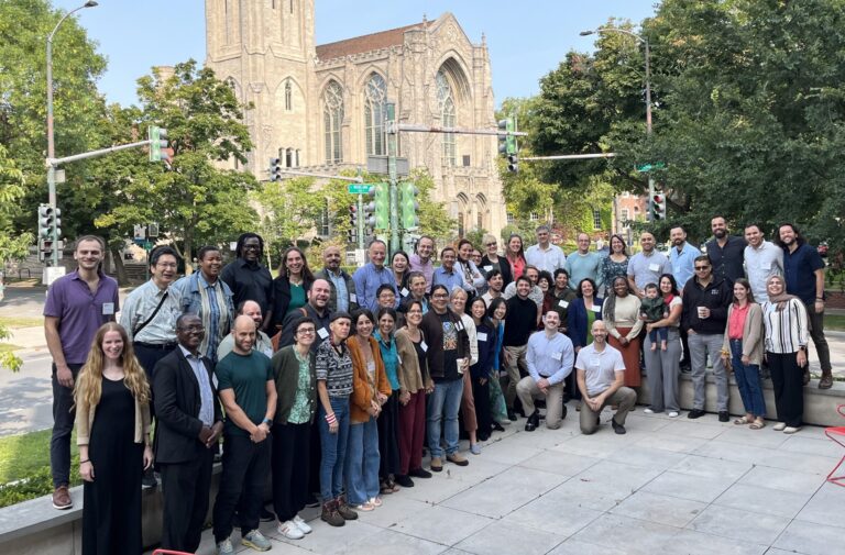 A group of several dozen people from around the world gather on a patio in Chicago as part of the group's 2024 seminar focused on conveying social concepts in the context of medical journal case studies.