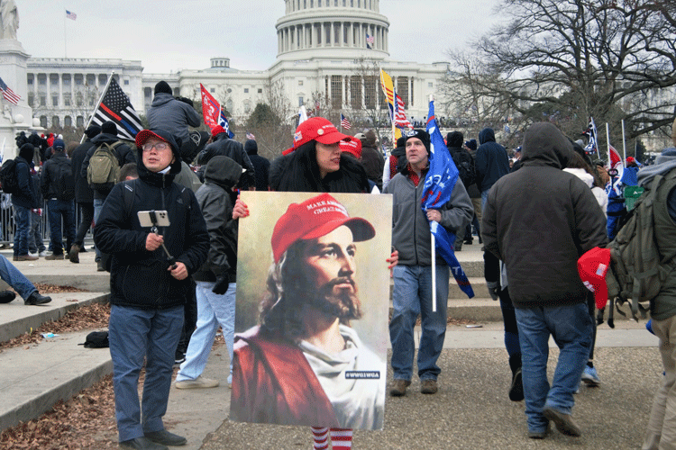 Outside the U.S. Capitol on Jan. 6, 2021, a woman carries a placard featuring Jesus Christ in a MAGA hat with a small QAnon emblem