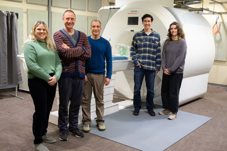 Five scientists stand in front of a large, white machine.