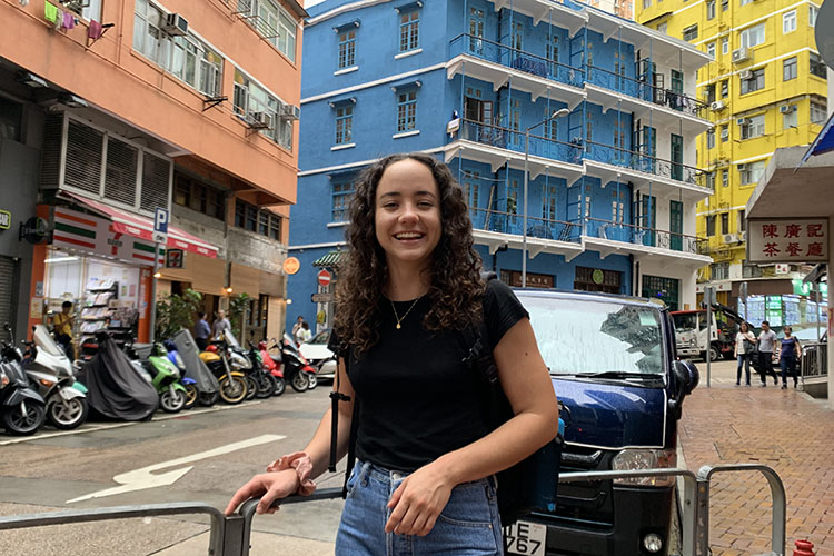 Maria Isabel Di Franco Quiñonez smiles while standing in front of colorful high-rise buildings.