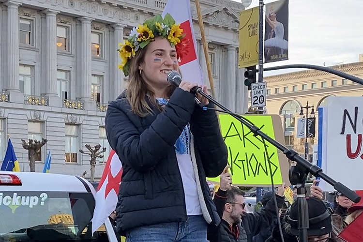 Marina Mezhibovsky, with a wreath of flowers on her head, speaks to a large pro-Ukraine rally in front of San Francisco City Hall