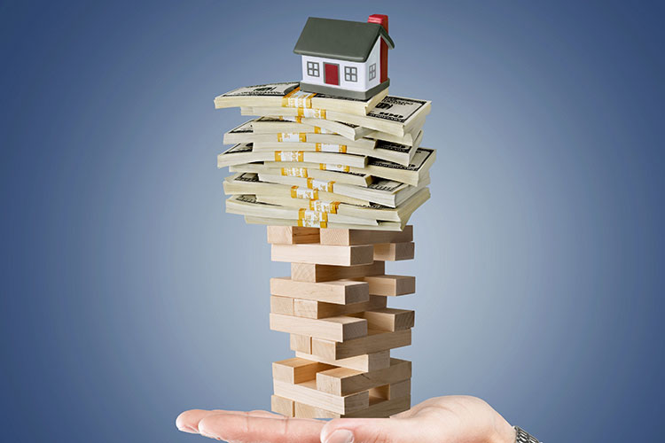 Graphic of a hand holding a house on top of a pile of a cash, both on top of a jenga set