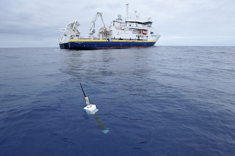 A small buoy floats in the ocean in front of a large ship