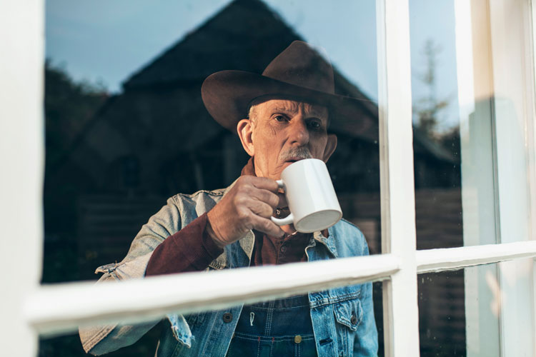 Old man with coffee cup staring out of window.