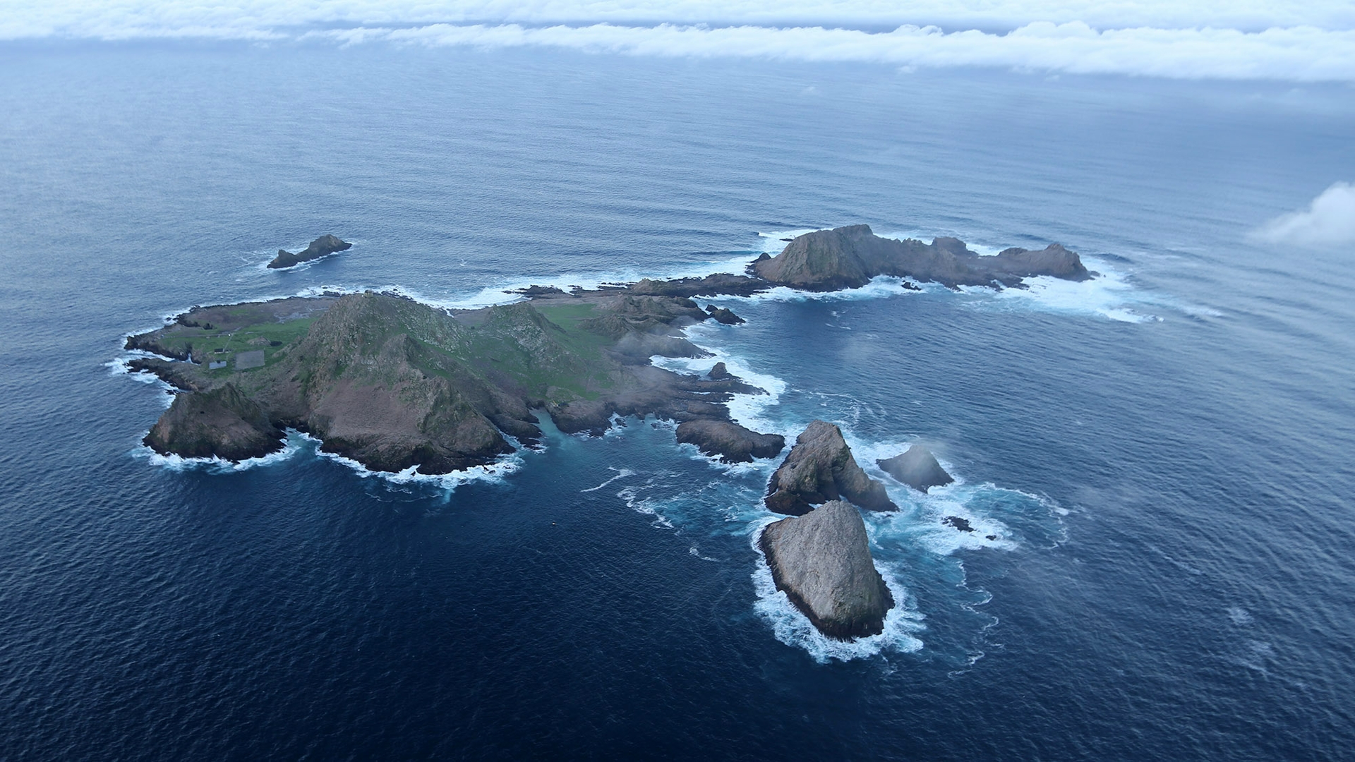 aerial view of rocky, treeless island withpatches of green and fog bank in background