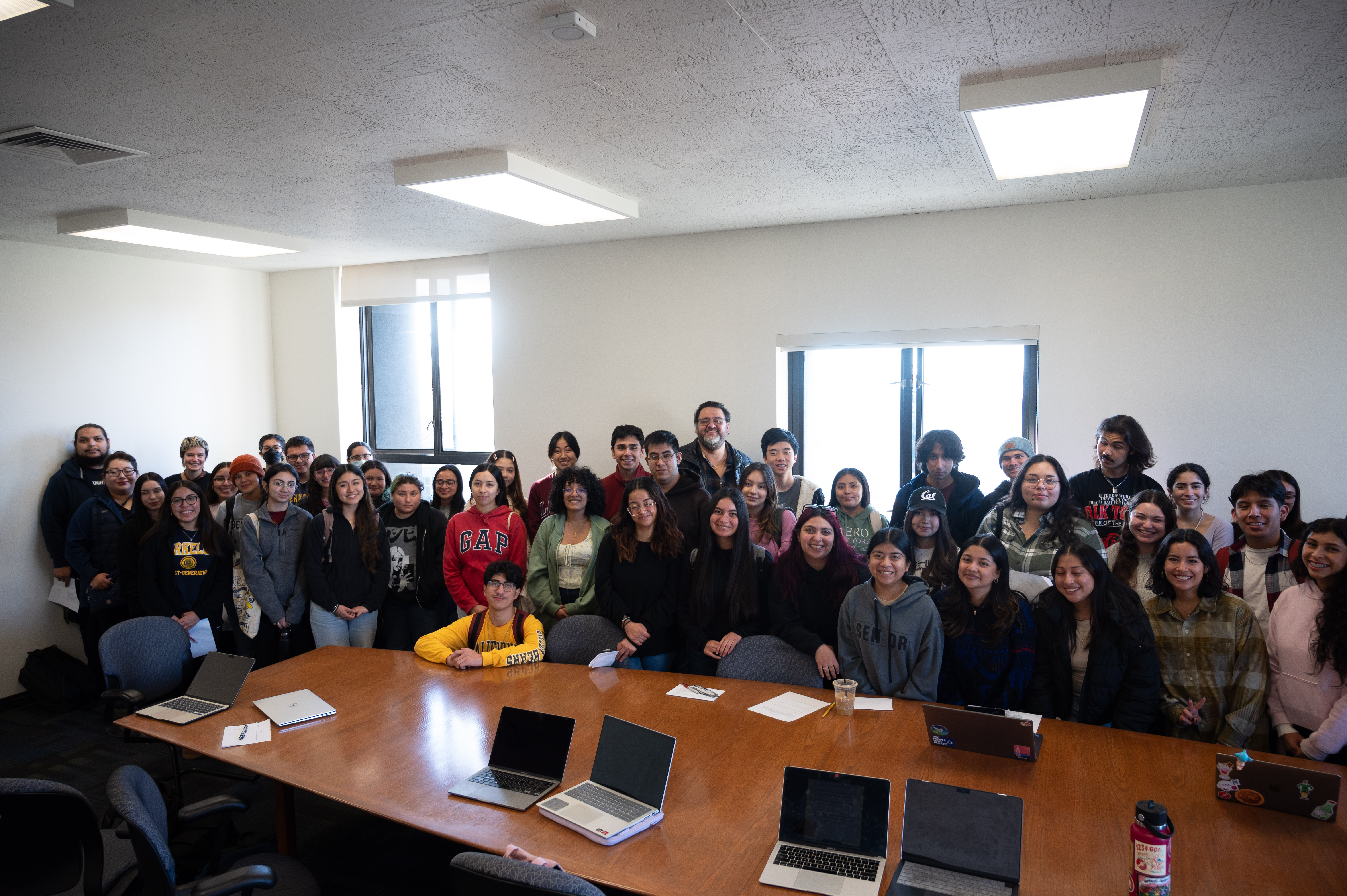A group of around 40 students pose with Pablo Gonzalez in a cramped room with a long brown conference table.