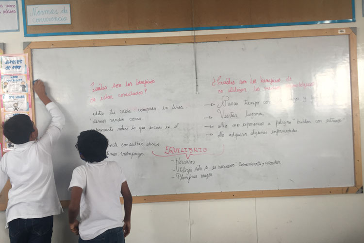 Two school students in Peru write on a white board.