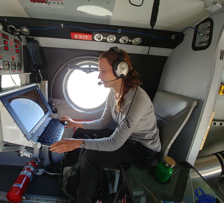 A photo of a woman hunched sitting at a computer wearing a headset.