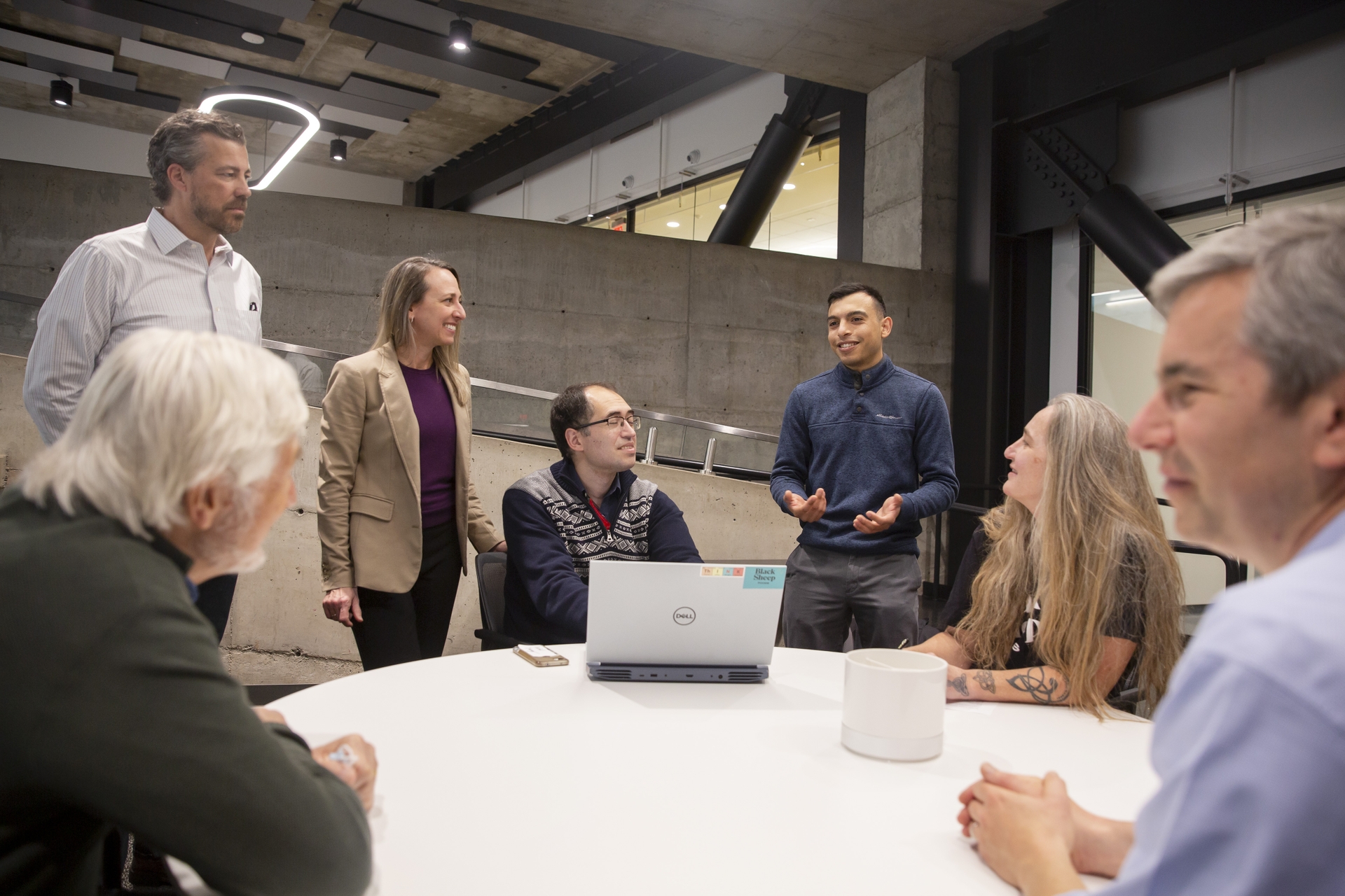 A group of people converse while gathered around a round table.