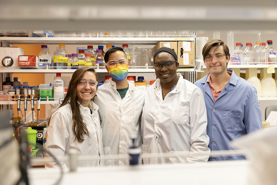 Four researchers posing in a lab wearing lab coats.