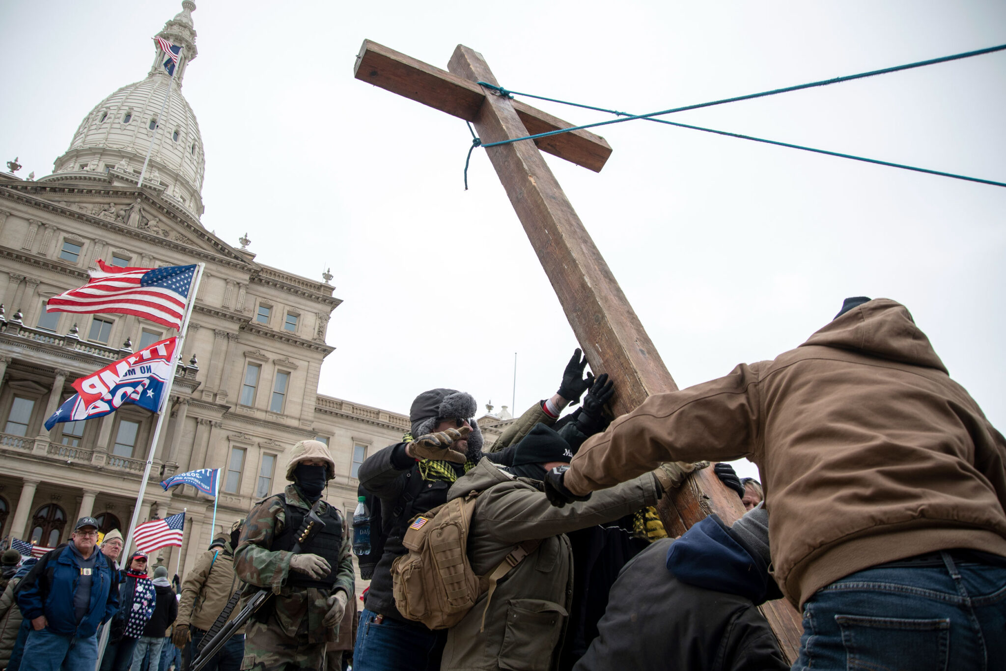 Members of the Proud Boys right-wing group, some of them dressed and armed for combat, raise a wooden cross outside the Michigan capitol.