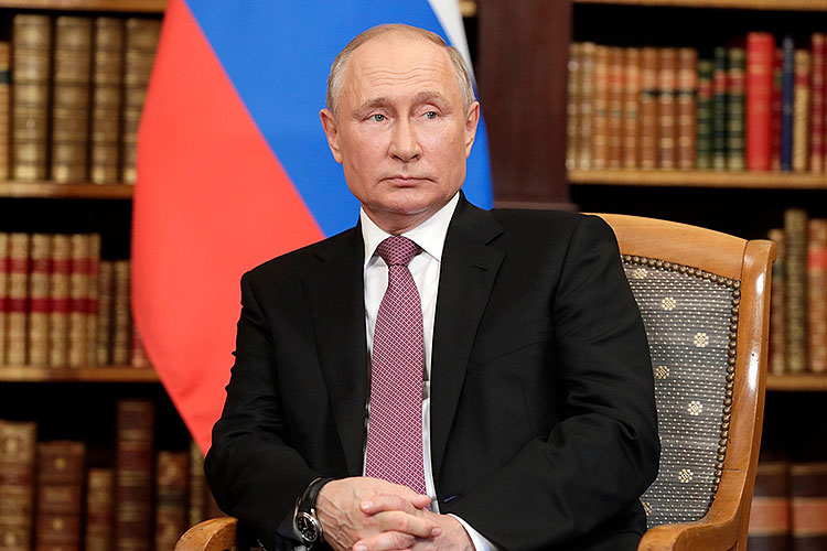 Russian President Vladimir Putin, seated before the Russian flag and a wall of old books
