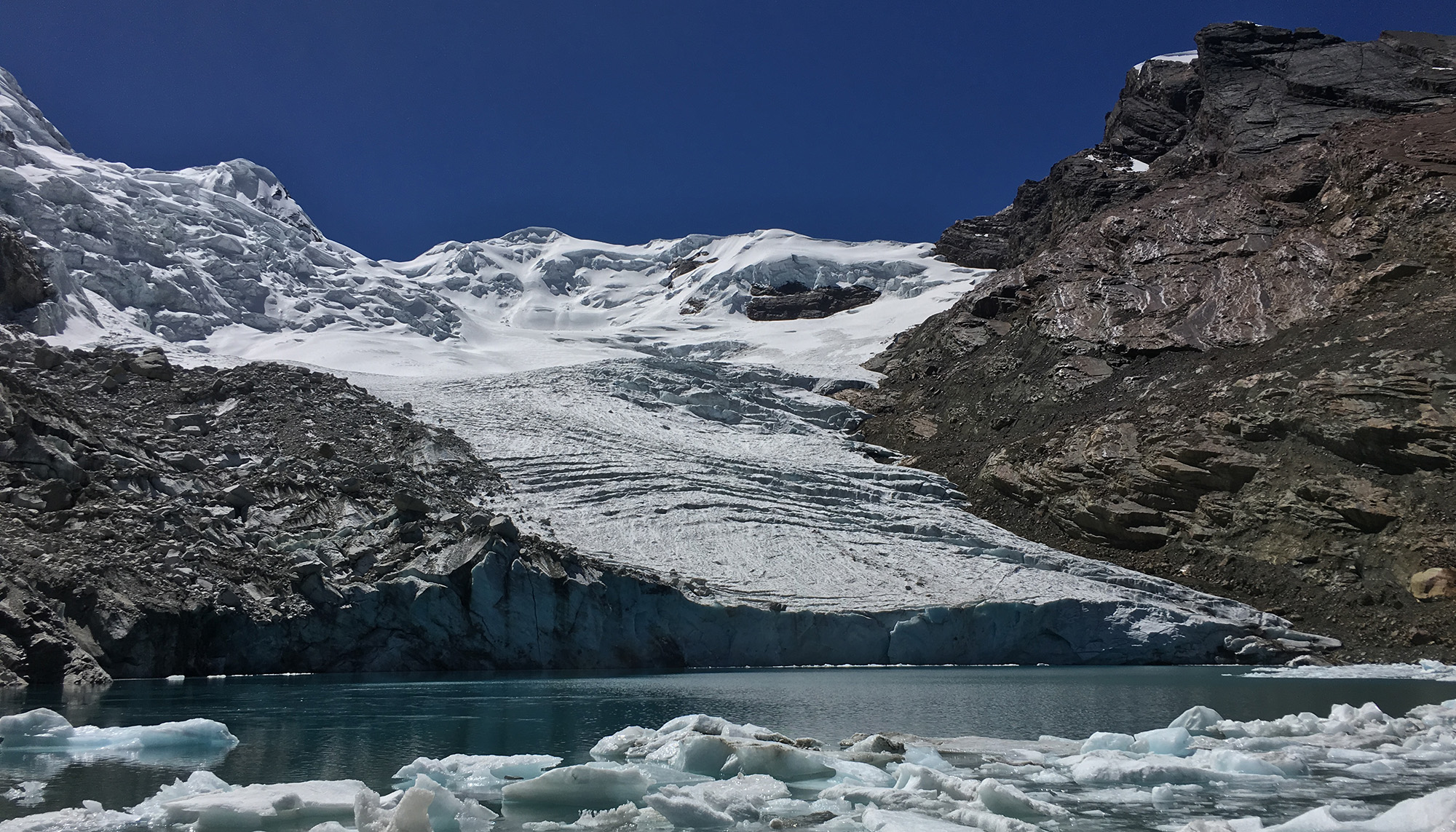 dirty white glacier ending at blue lake with deep blue sky above