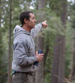 A photo of Rob York in the forest, pointing at some trees