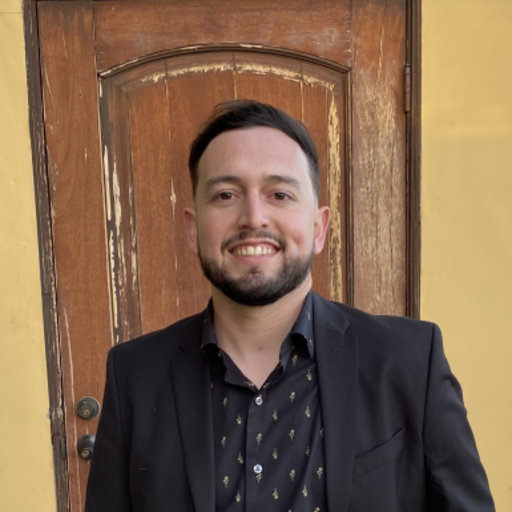 smiling man in dark blue shirt and jacket in front of brown weathered door