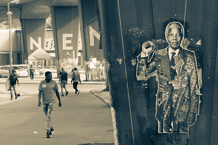 ooster of Nelson Mandela on a pillar with people walking along nearby street
