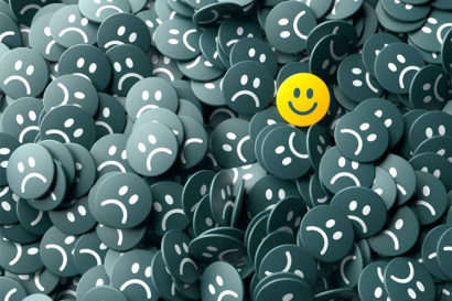 Pile of buttons; all of them have sad faces on them but there is one button with a smiley face
