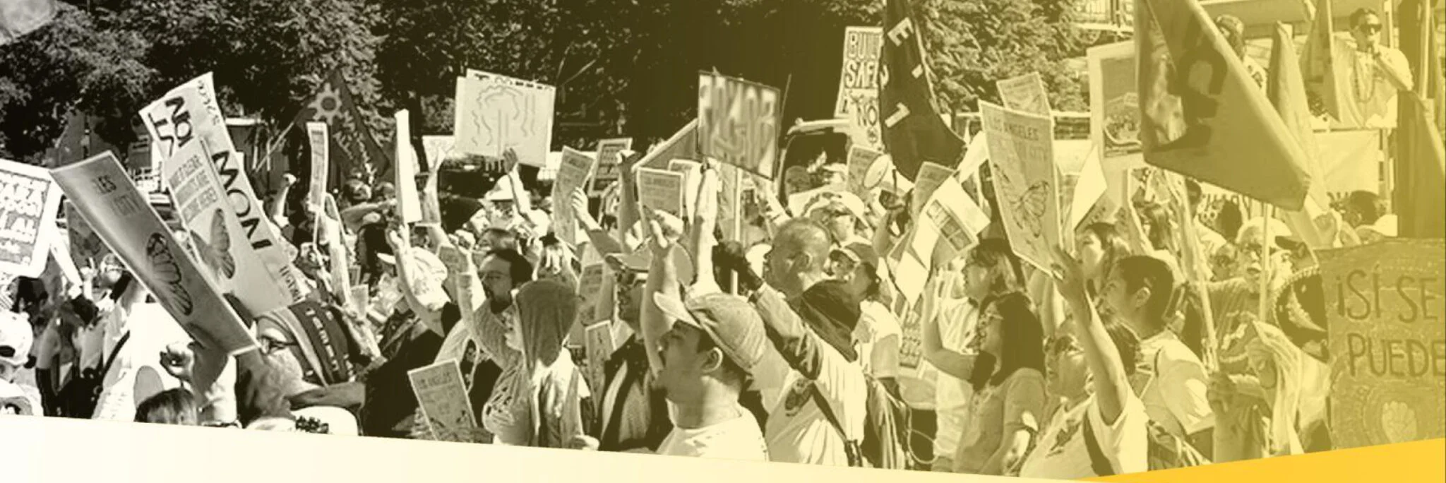 Black and white photo of protest march, with sideview of people marching and holding Spanish-language signs including si se puede.