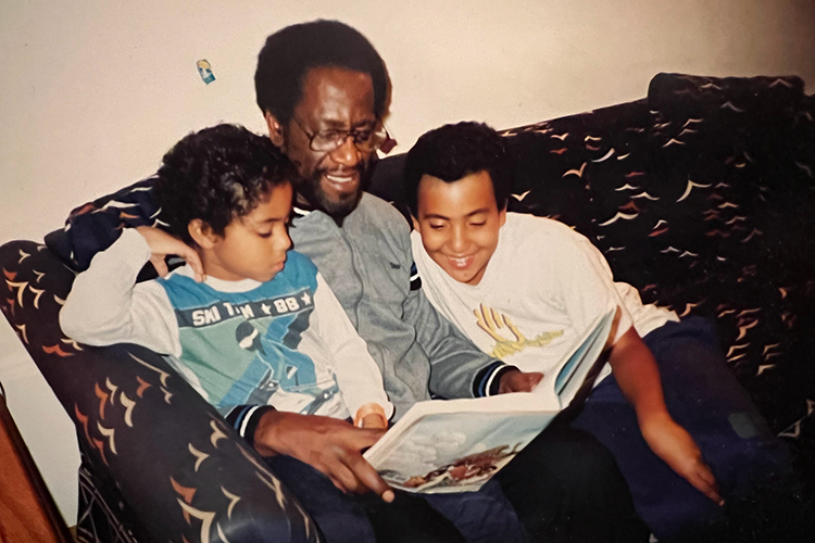 Old photo of Aaron Streets as a kid reading a book with his dad on brother on a couch.