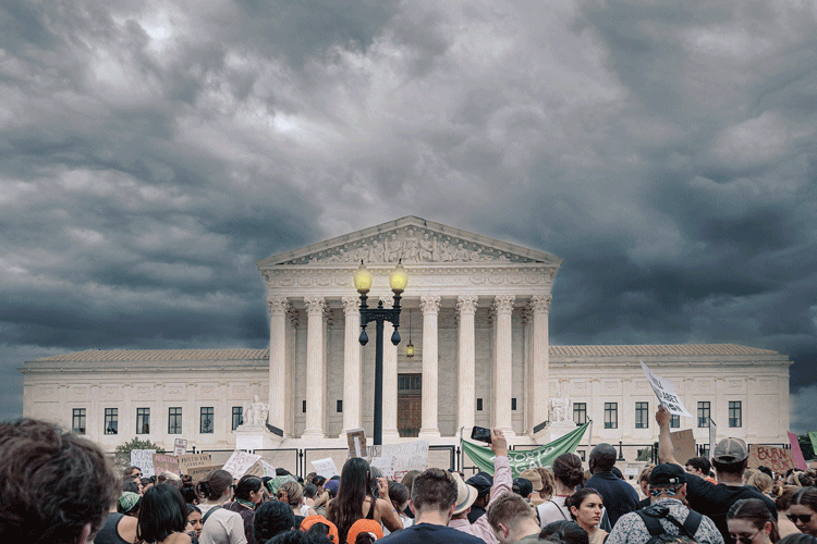 The U.S. Supreme Court building, with intensely stormy skies above and protests swirling below