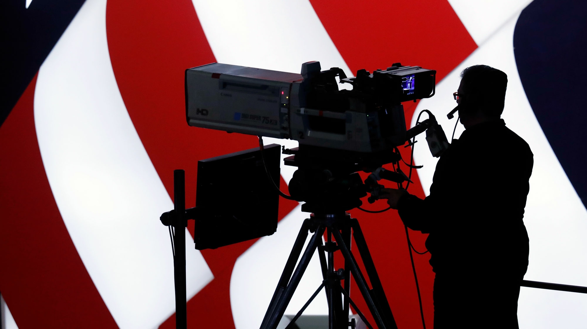 A television cameraman in silhouette against a U.S. flag suggests the deep importance of television advertising in political campaigns