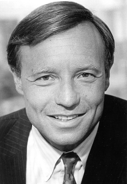 a black-and-white photograph of a man smiling softly and wearing a suitjacket