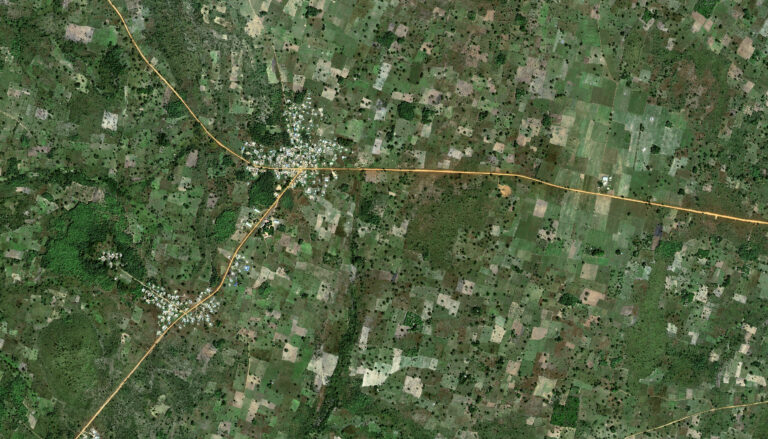 A satellite image taken far above the village of Kalanga, Togo, surrounded by a checkerboard of fields in various shades of green and brown