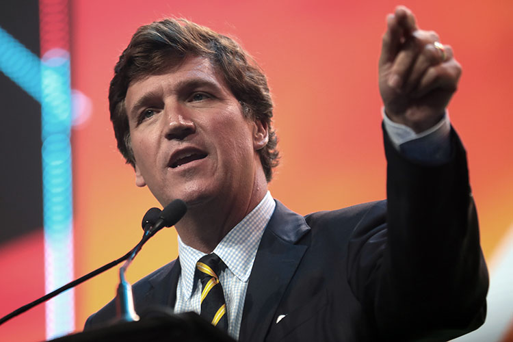 Tucker Carlson gestures during a talk, with a brightly-colored abstract backdrop