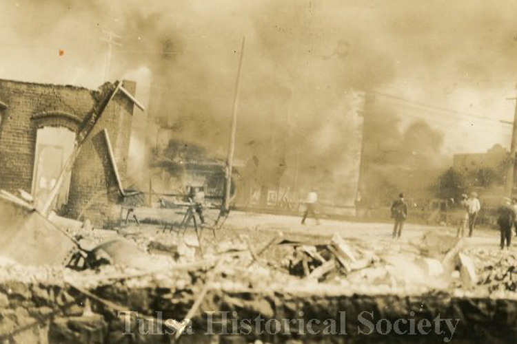 sepia toned photo of burning buildings with people looking on