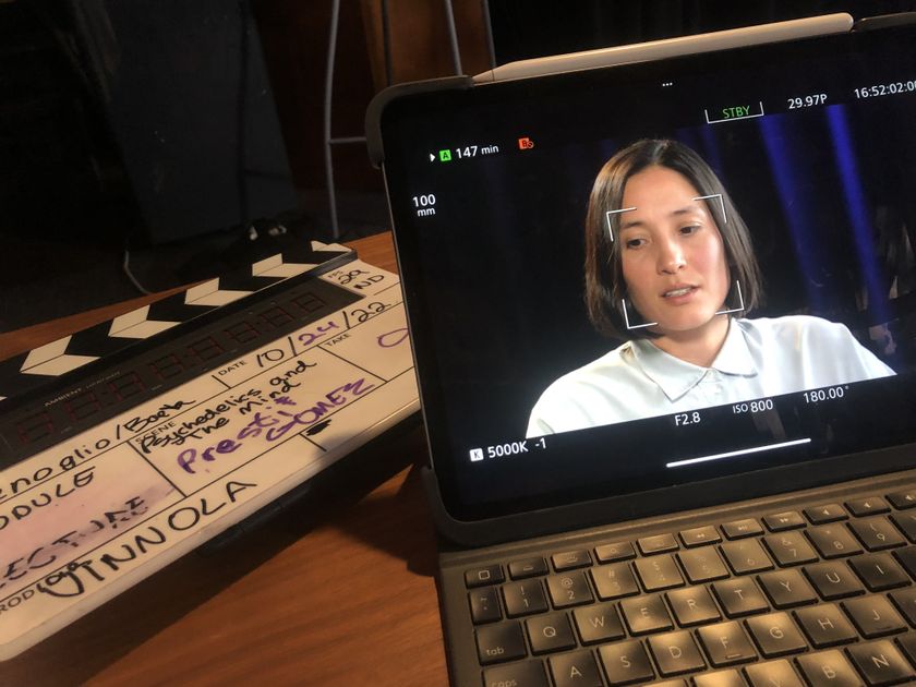 An image of a person with shoulder-length hair being interviewed on a computer screen next to a video clapperboard