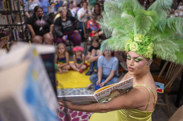 image of a drag queen in a green feather headress reading a book to a group of children